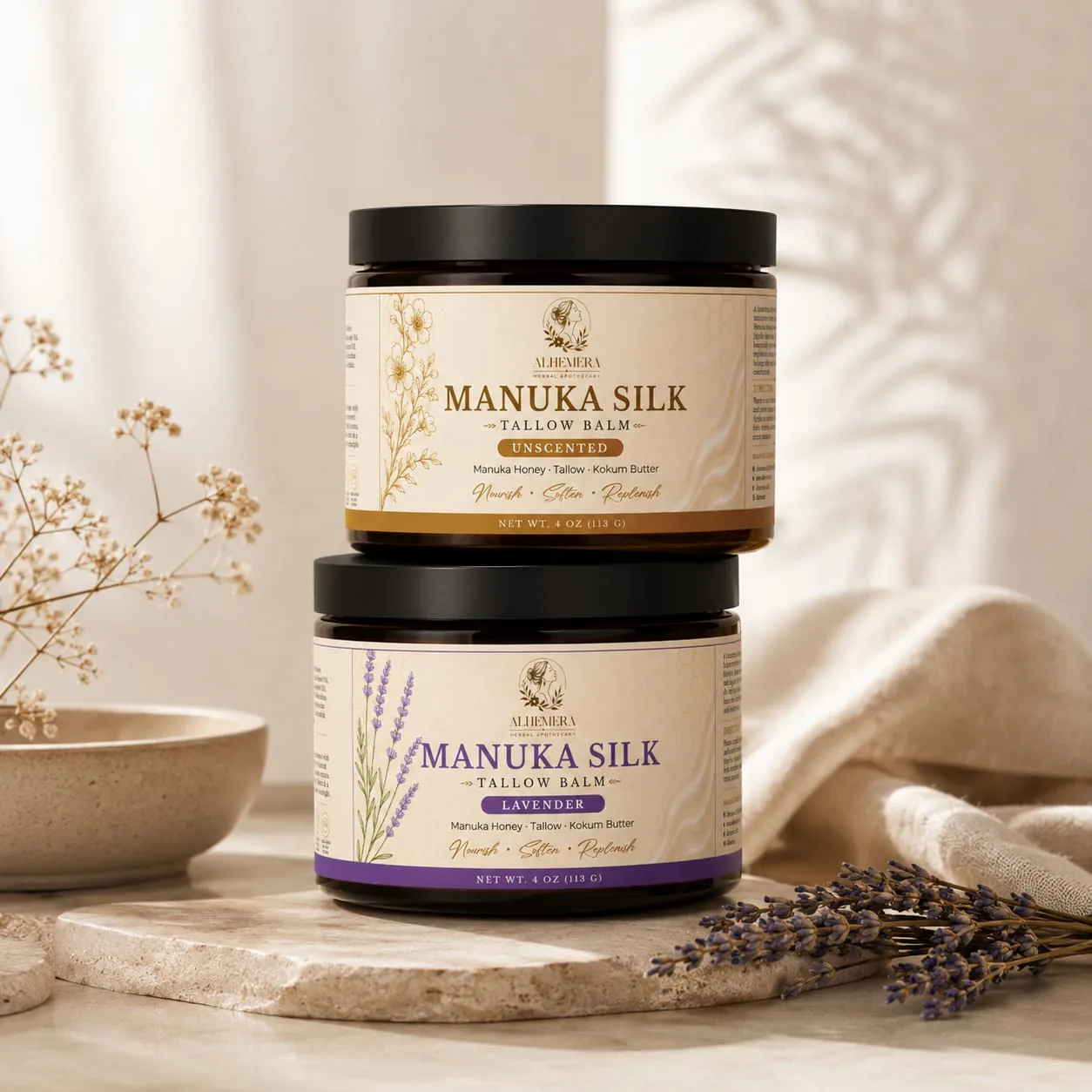 ALHEMERA Manuka Silk Tallow Balm in two stacked amber jars, lavender and unscented, on a travertine dish with dried lavender and linen